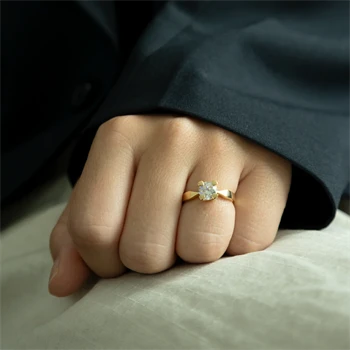 Hånd med elegant guldring, central sten i prongfatning. Skinnende, glat ringbånd.